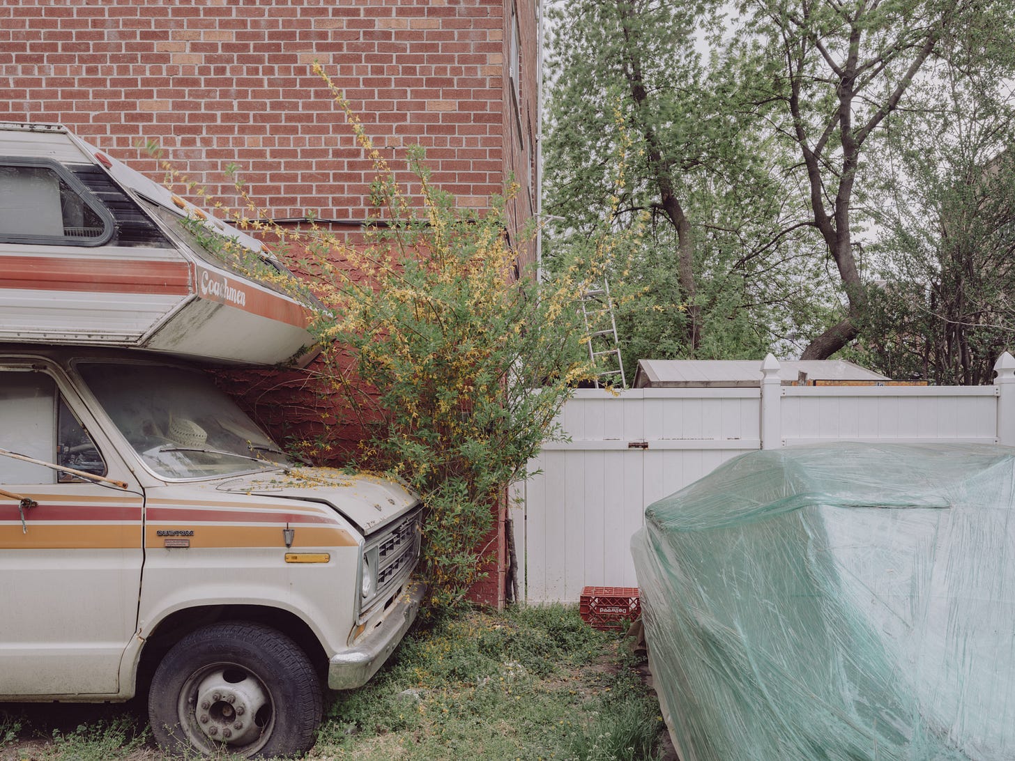 Front-half-of-camper-van-next-to-forthsyia-and-car-wrapped-in-green-plastic