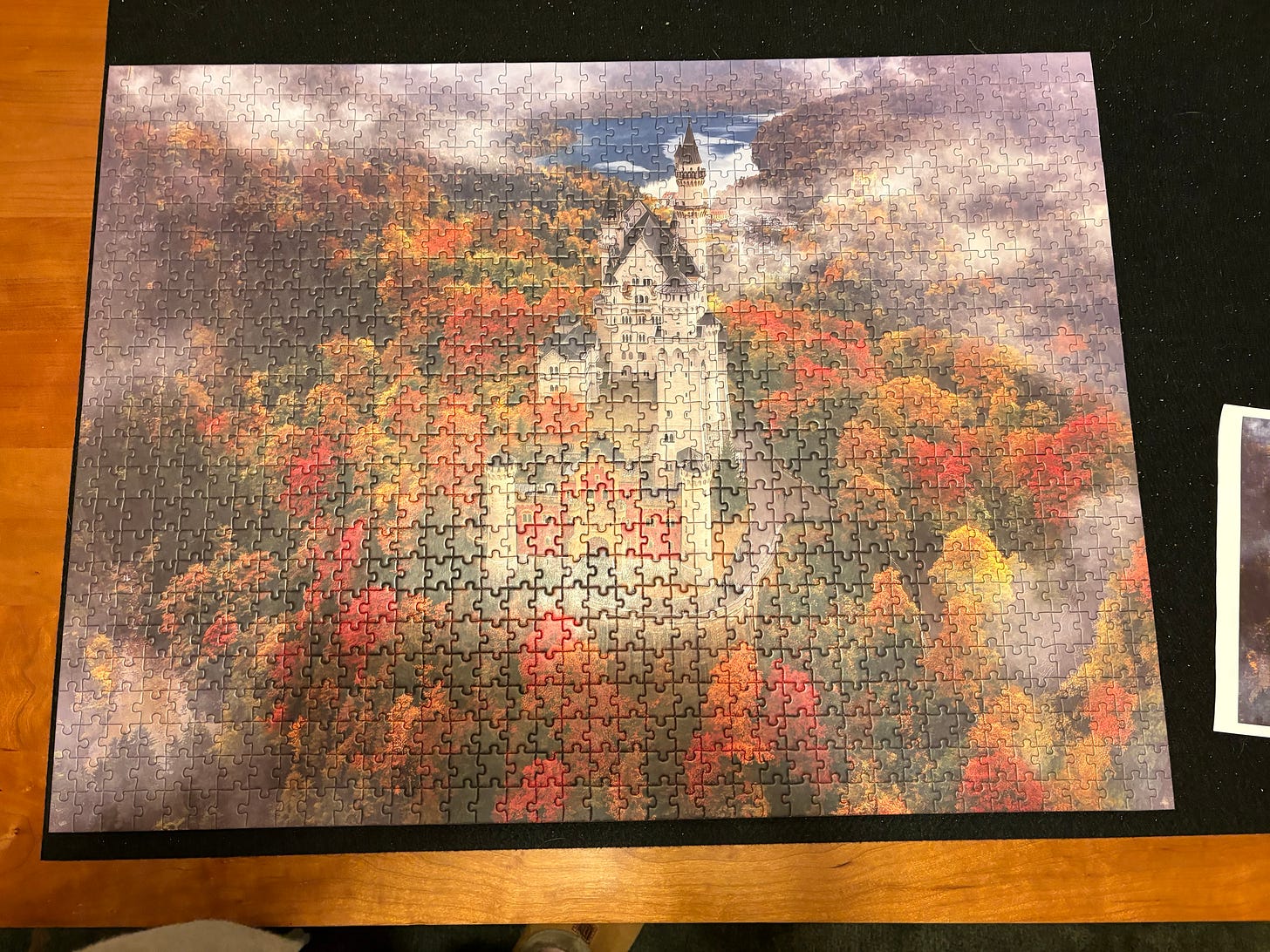 A completed 1000-piece jigsaw puzzle. The image is of Neuschwanstein Castle surrounded by trees with autumn foliage. 