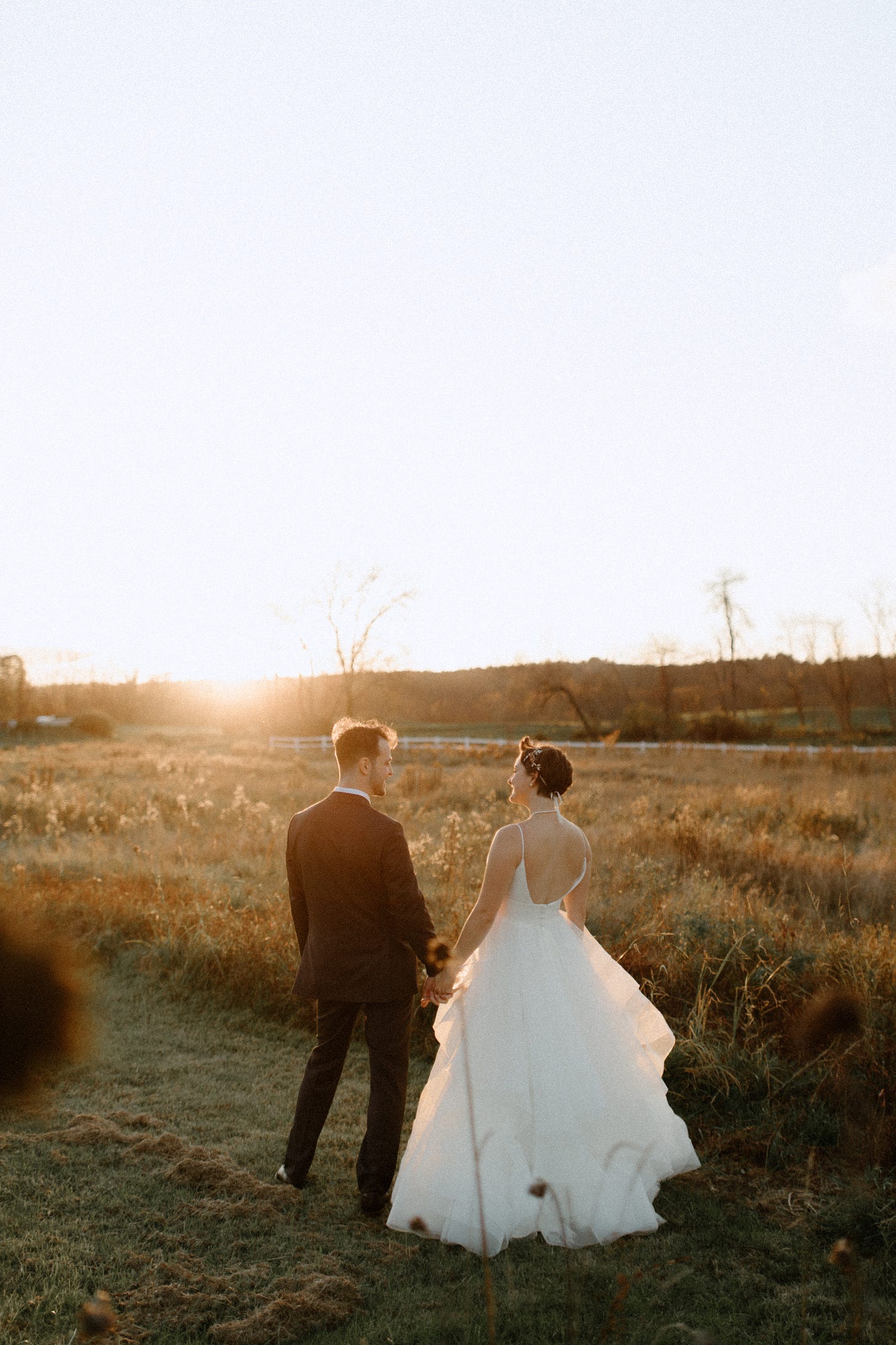 photo of author and husband on wedding day looking out over a field while holding hands