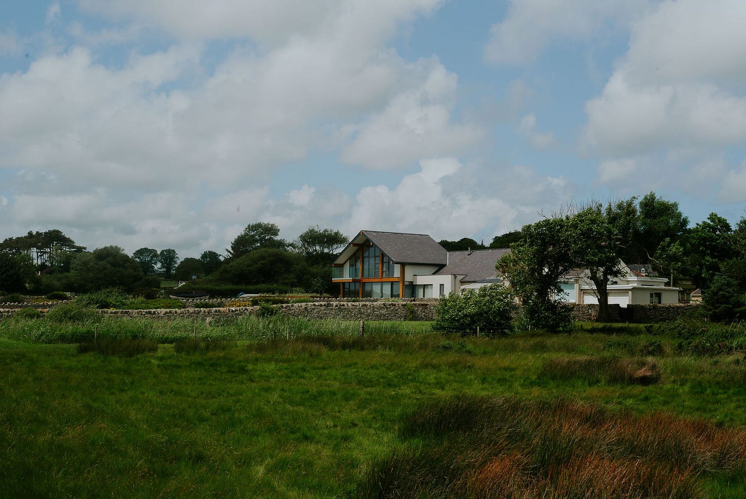 A nicely designed house sits next to a green field. The architecture is quite modern compared to the traditional buildings in Wales.
