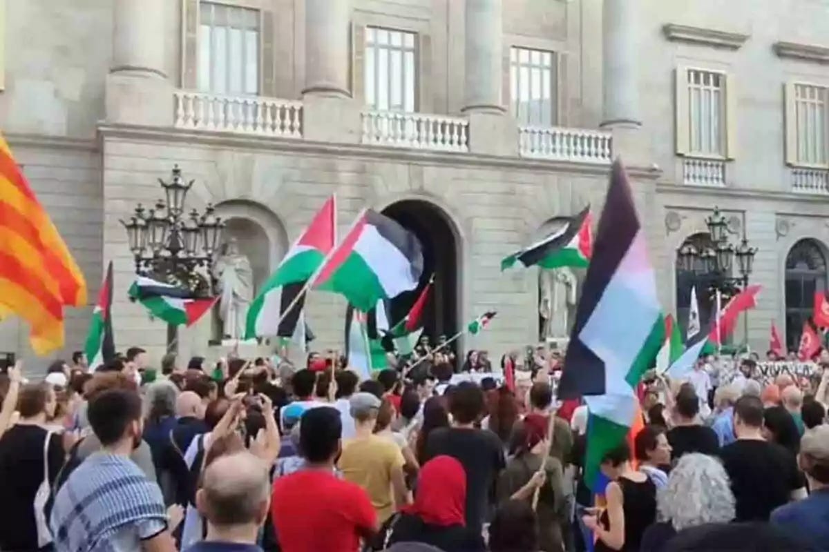Una multitud es reuneix davant d'un edifici històric, onejant banderes de diferents colors. Una multitud es reuneix davant d'un edifici històric, onejant banderes de diferents colors.