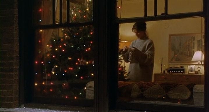 This may contain: a woman standing in front of a christmas tree looking out the window at her reflection