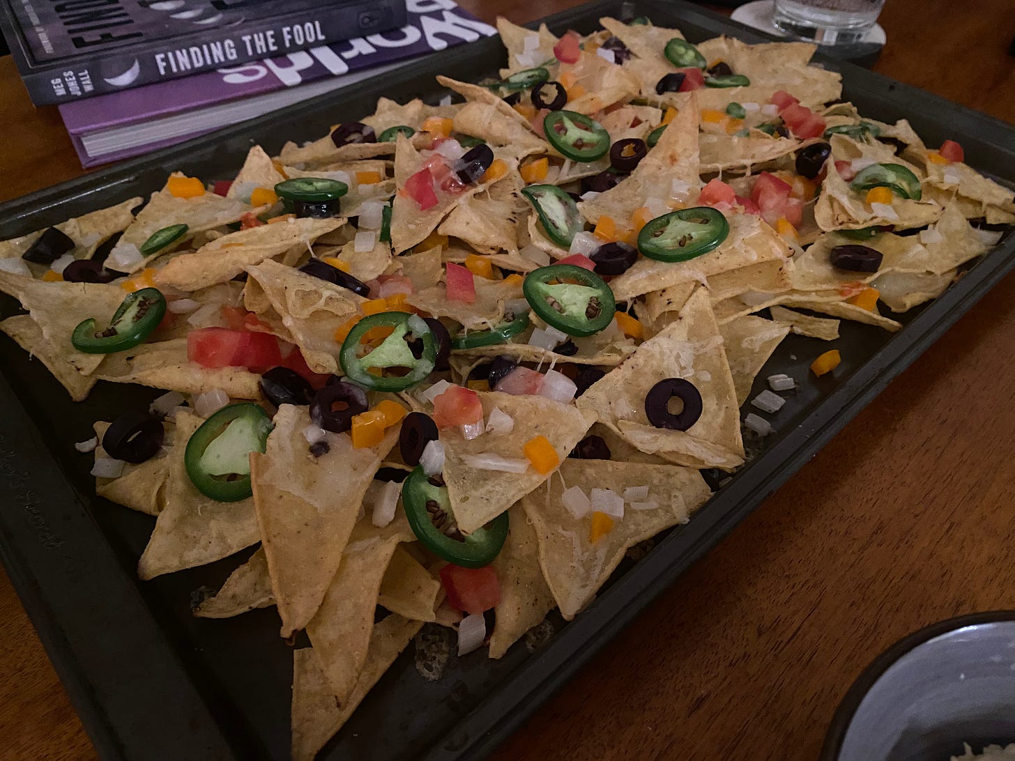 A sheet pan of nachos with olives, cheese, peppers, onions, jalapeños, and tomatoes.