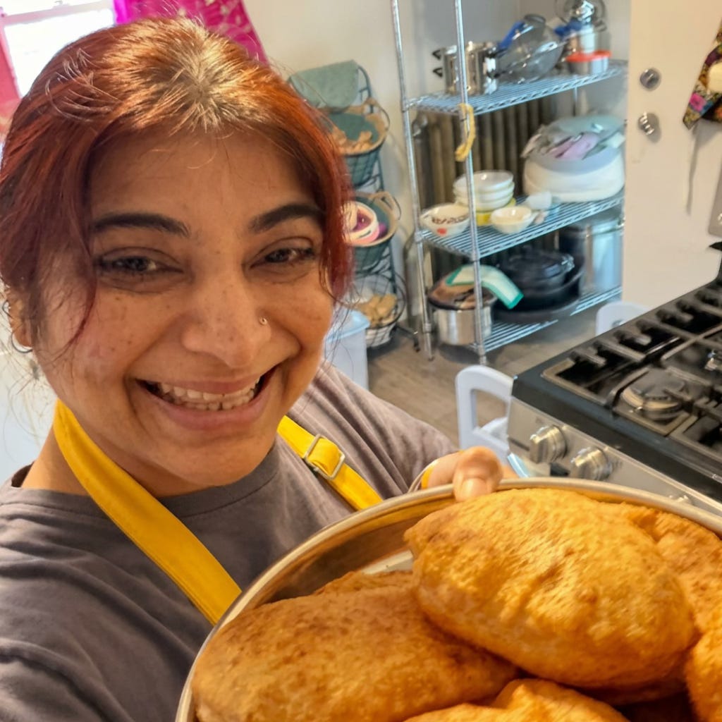 Chef Daljeet smiling in her kitchen holding a plate of freshly made puris.