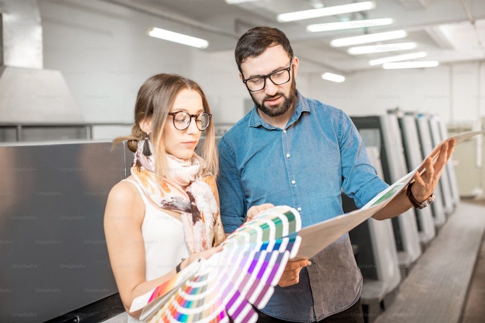Young woman designer and print operator working together with color swatches standing at the print manufacturing