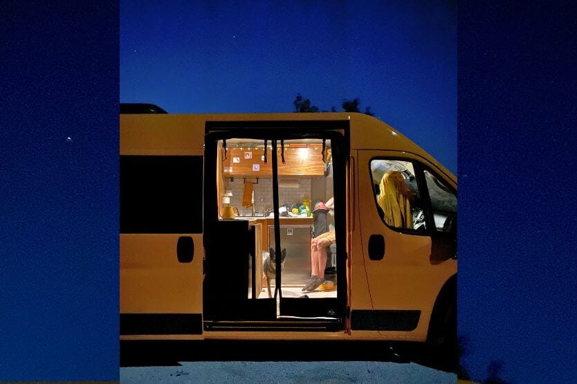 Our bright yellow campervan sits against the starry night sky, lit up from within with cozy warm lighting