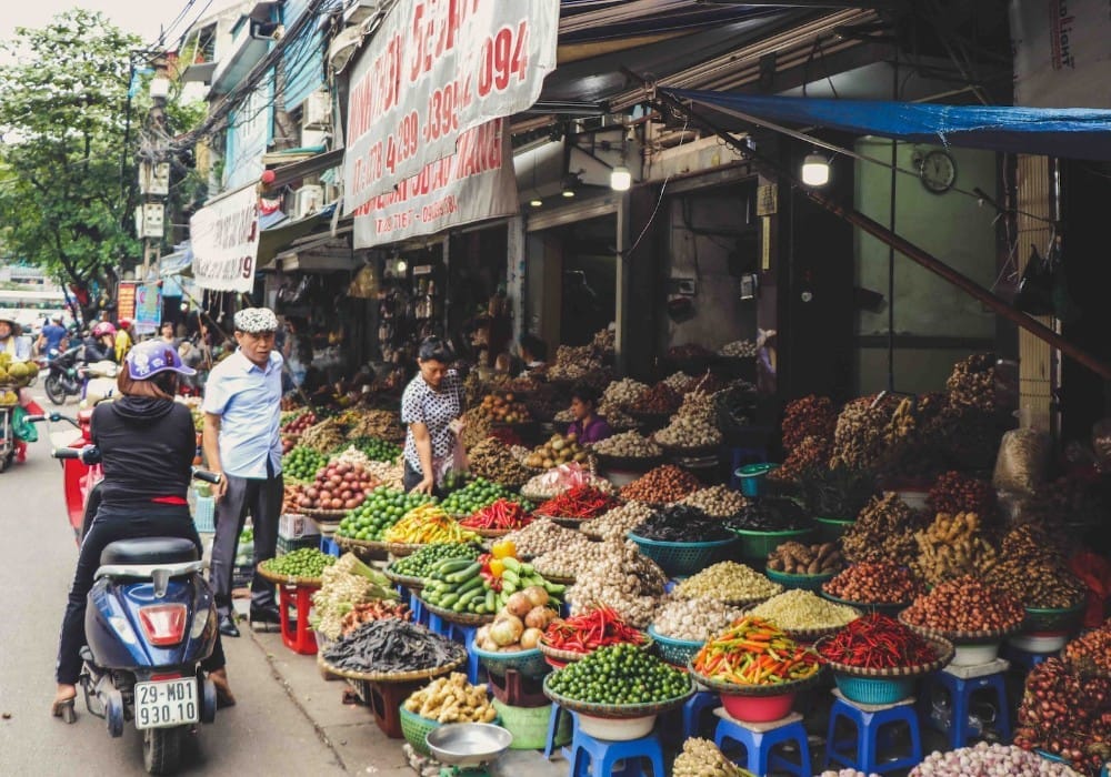 Asian woman on a scooter at an outdoor fruit and vegetable market full of high vibration foods