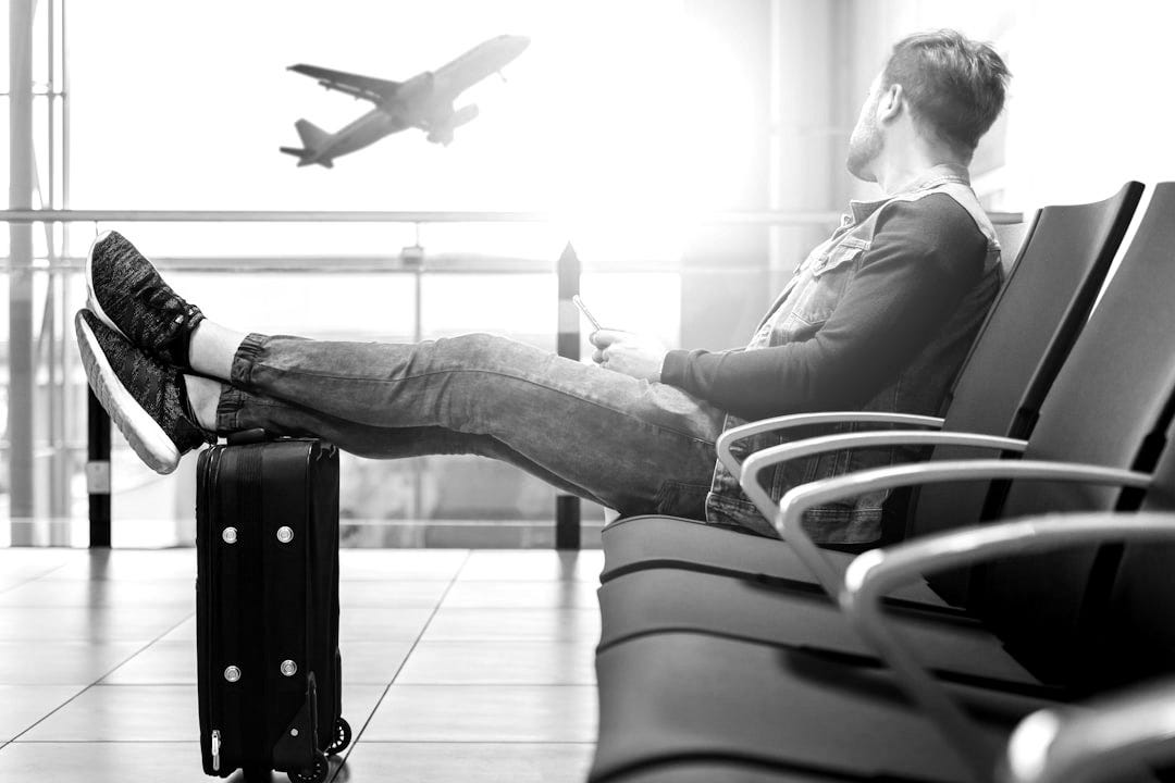 man sitting on gang chair with feet on luggage looking at airplane man sitting on gang chair with feet on luggage looking at airplane