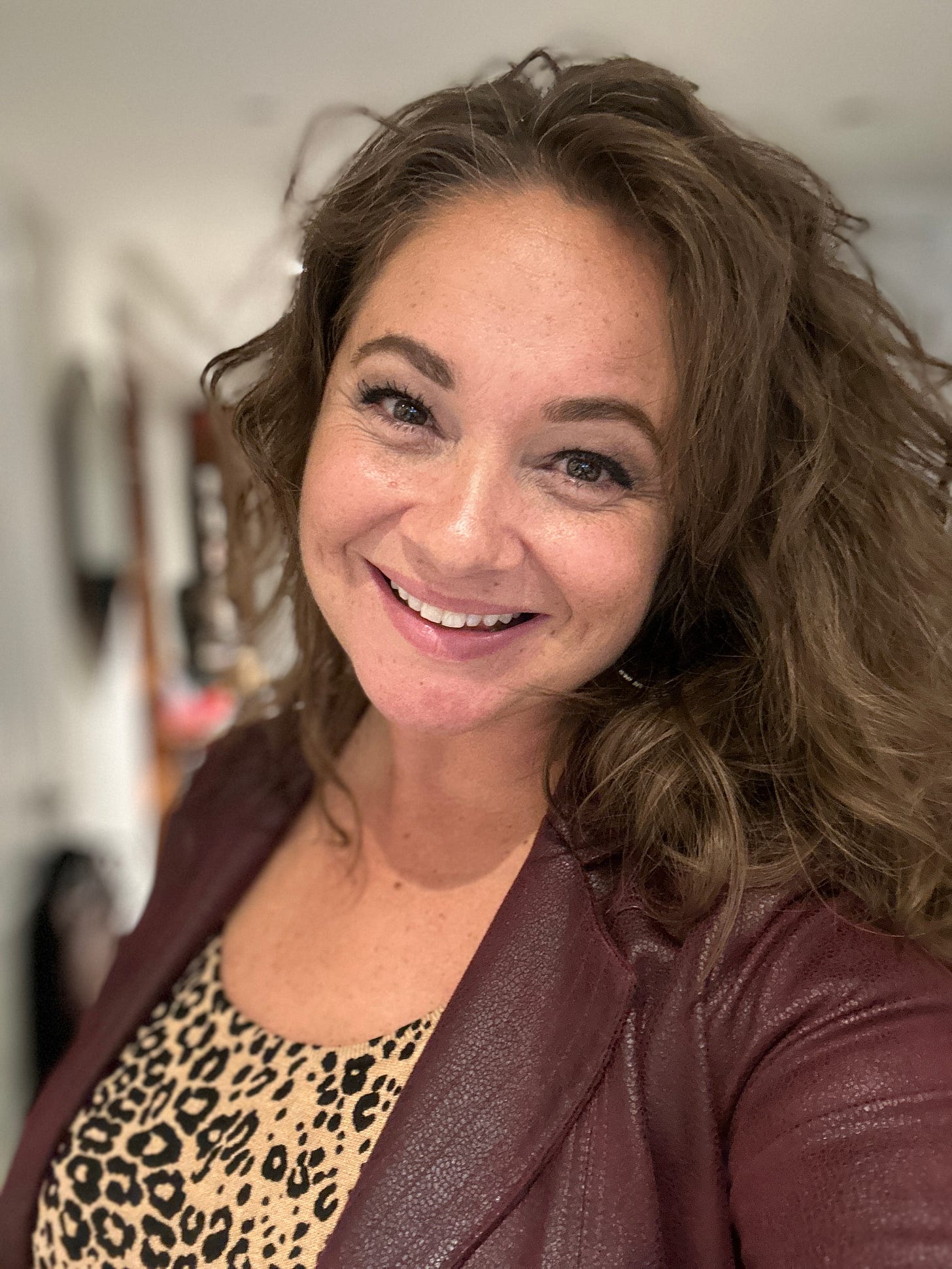 Stephanie Edward is a white woman with brown hair and brown eyes. She is wearing a wine-coloured blazer and leopard-print top and is smiling at the camera.
