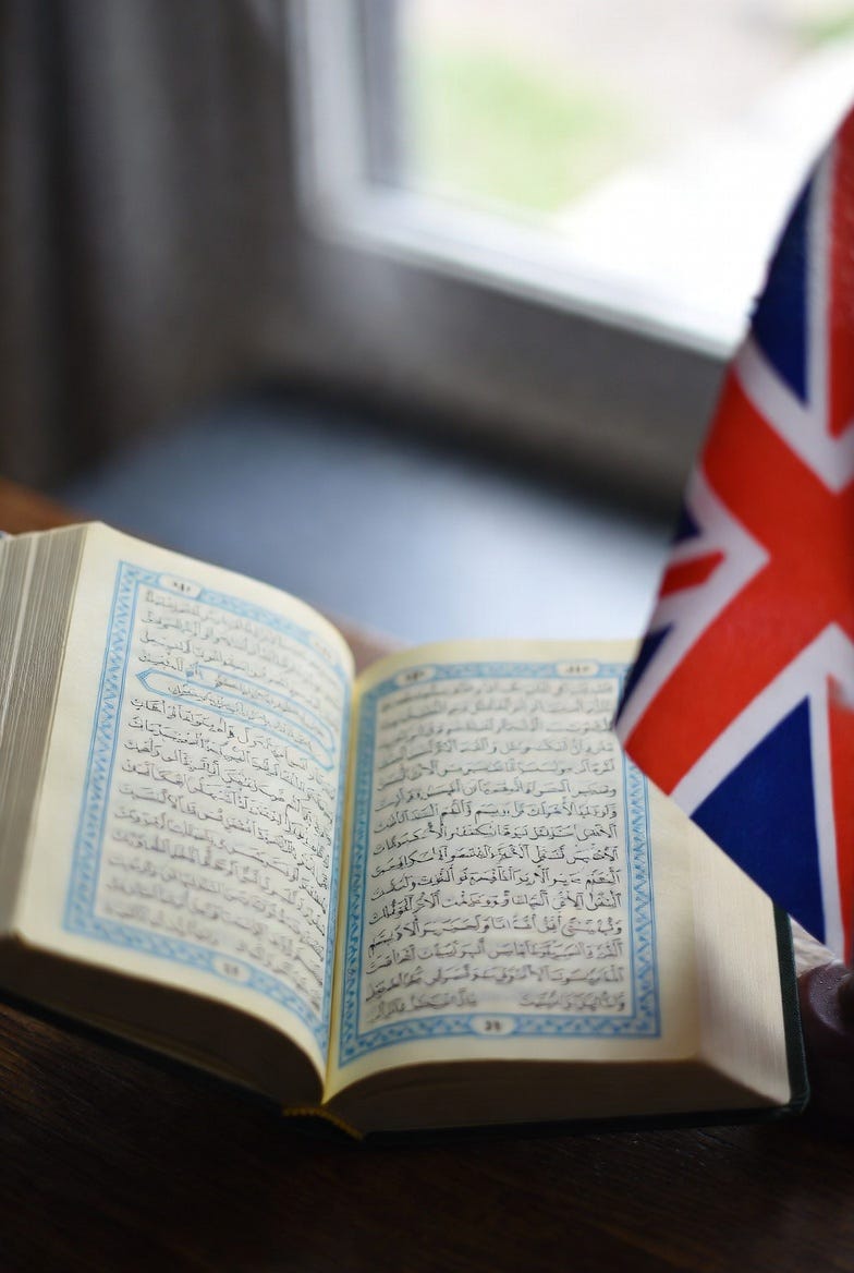 A photograph of an open Quran and a UK flag in a serene indoor setting. A photograph of an open Quran and a UK flag in a serene indoor setting.