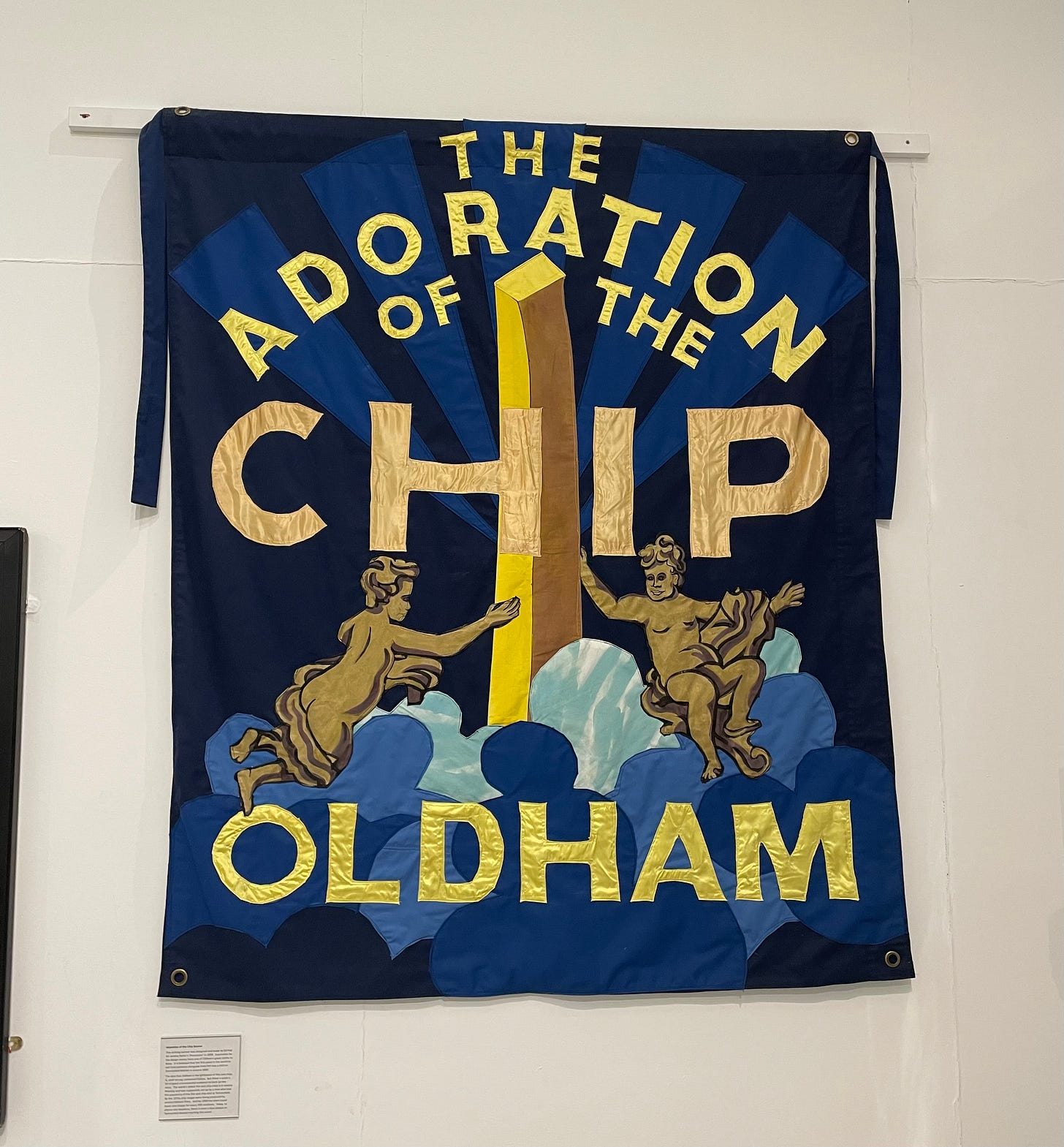 A banner bearing the legend 'The adoration of the chip' depicting two cherubs on a blue background worshipping a giant potato chip. 