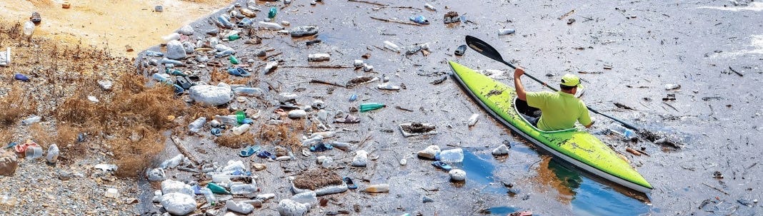 A man in a yellow kayak on a river filled with trash