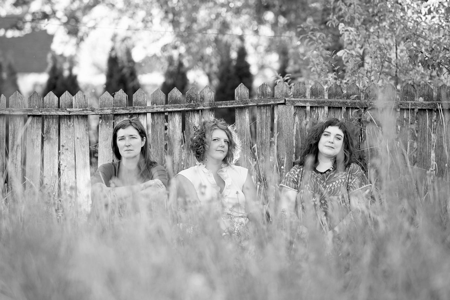 black white photo of three women in front of a fence