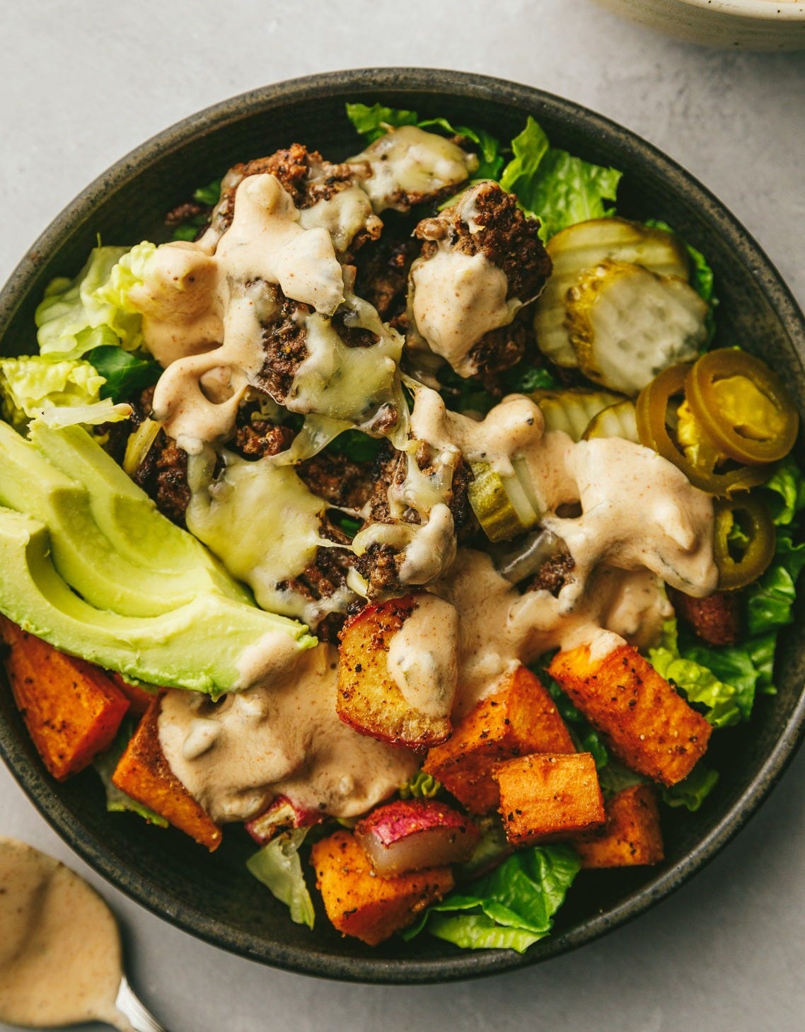 A burger bowl with creamy chipotle sauce and burger toppings.