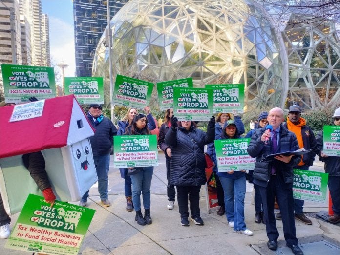 Ron Davis holds a microphone and a house mascot and a dozen sign wielding advocates standing in front of the glass spheres.