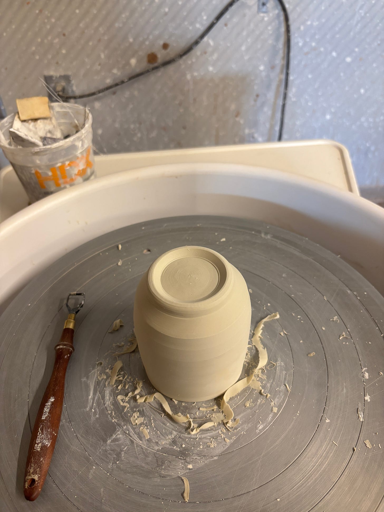 upside down freshly trimmed cup with foot on wheel. next to it is a rosewood trimming tool. 