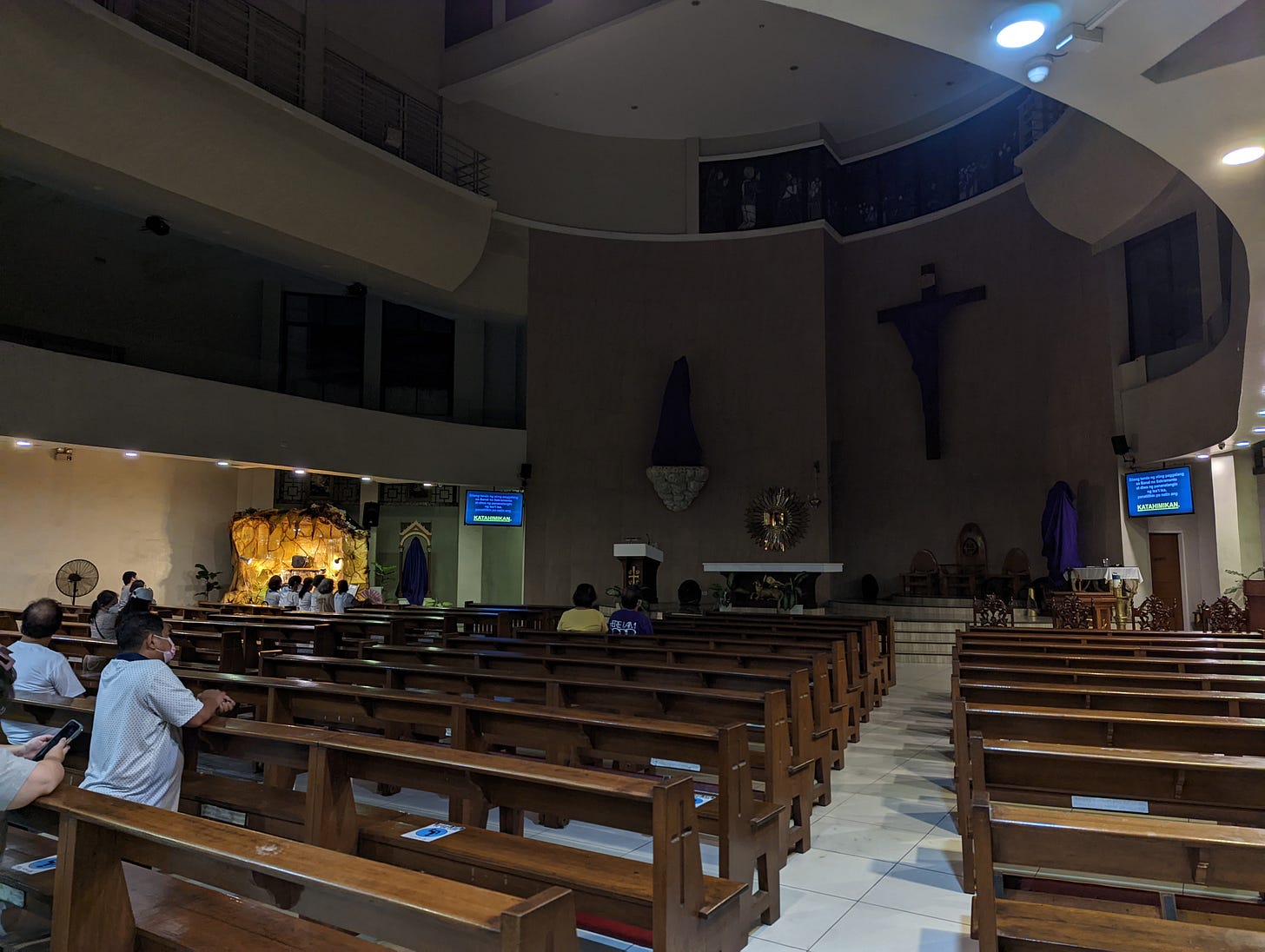 The mostly dark interior of the Our Lady of Fatima Parish with a few visitors in view