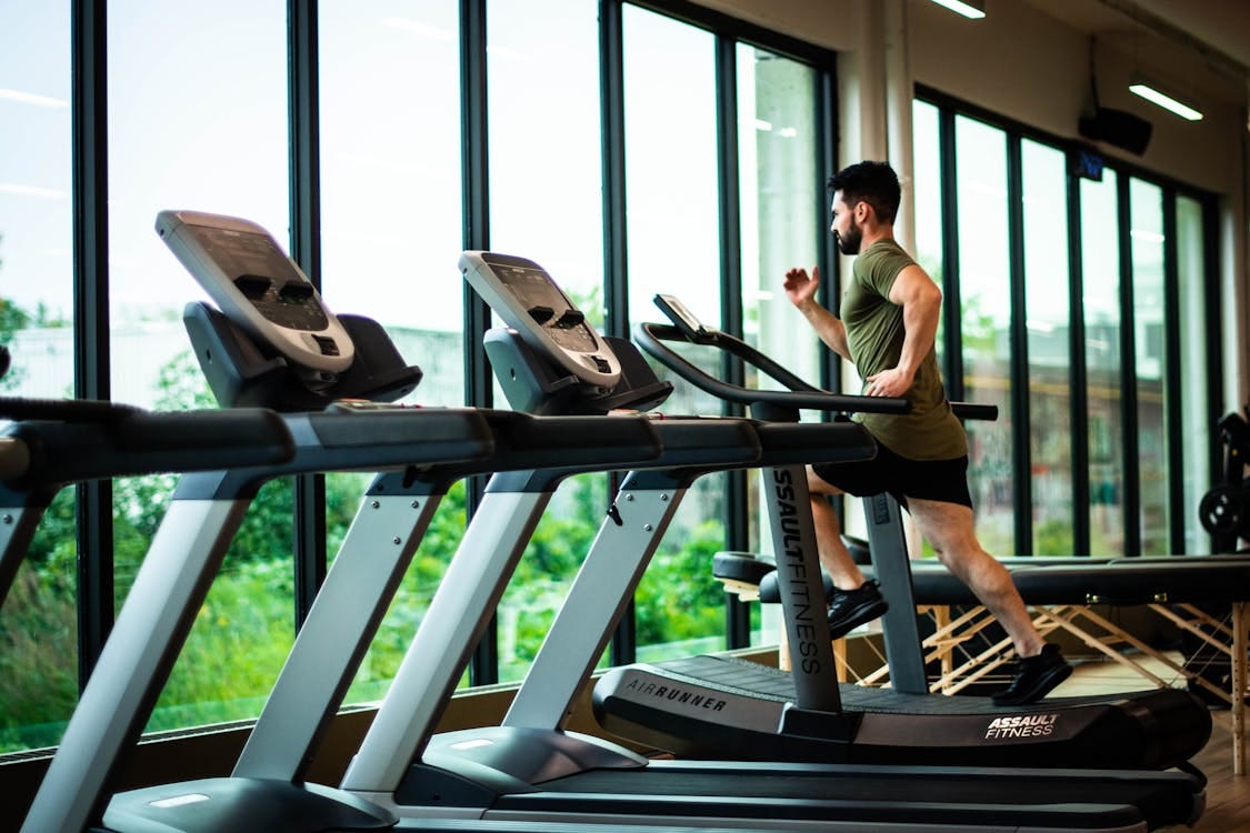 Free Young man workouts on treadmill in modern gym with large windows and natural light. Stock Photo