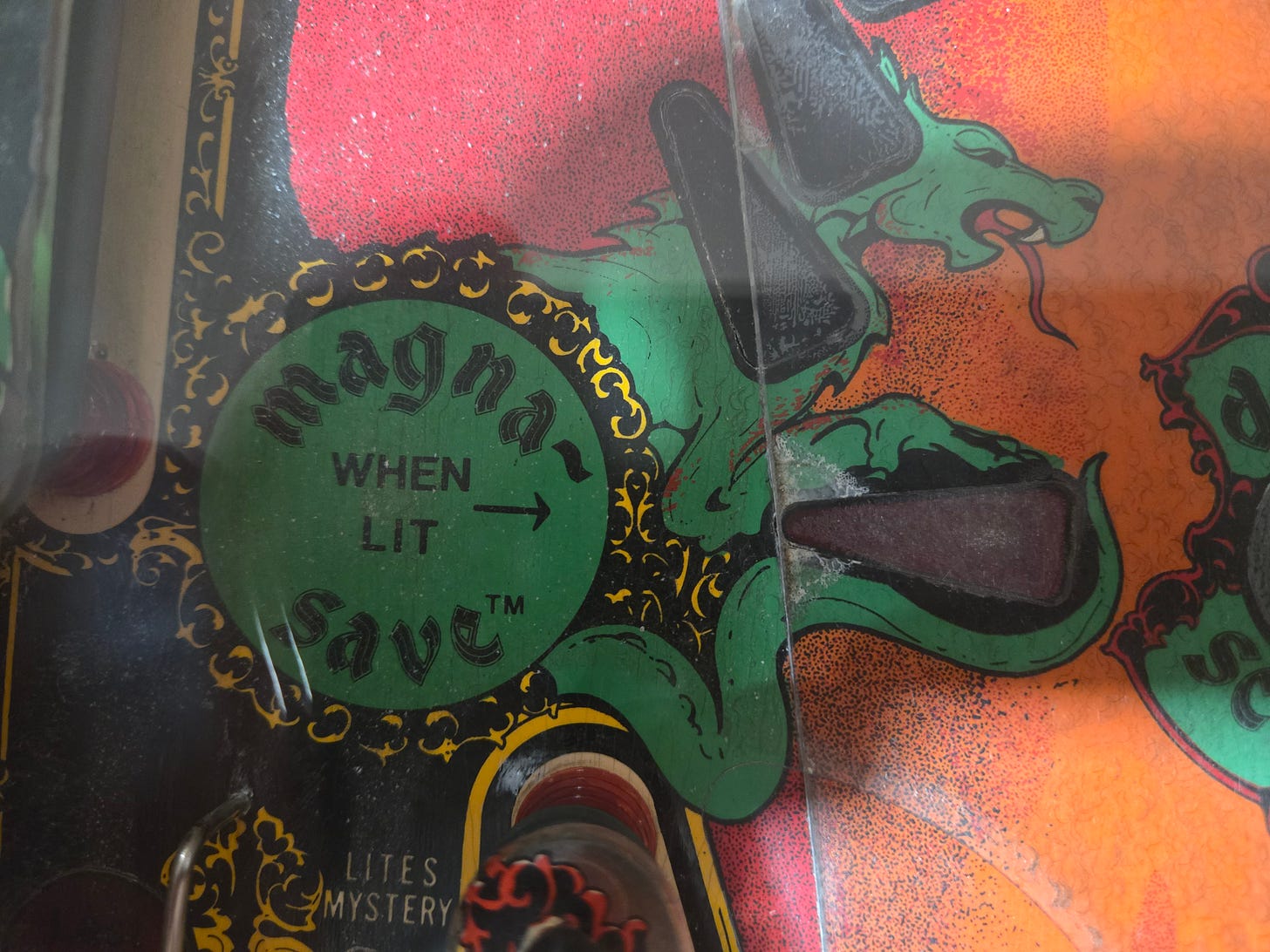 Close-up of the Magna-Save insert on the Black Knight (1980) playfield showing the 'Magna Save WHEN LIT' label with dragon artwork Close-up of the Magna-Save insert on the Black Knight (1980) playfield showing the 'Magna Save WHEN LIT' label with dragon artwork