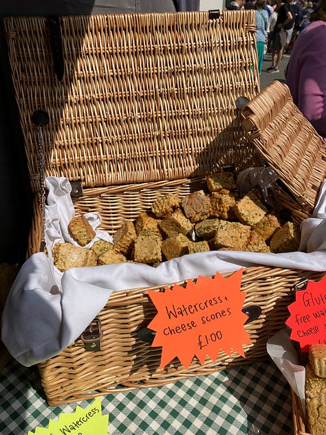 Picnic hamper filled with dozens of watercress & cheese scones; a Hey Duggee balloon looking especially happy above a stall selling watercress-inspired burgers, and the festival banner against a blue sky.
