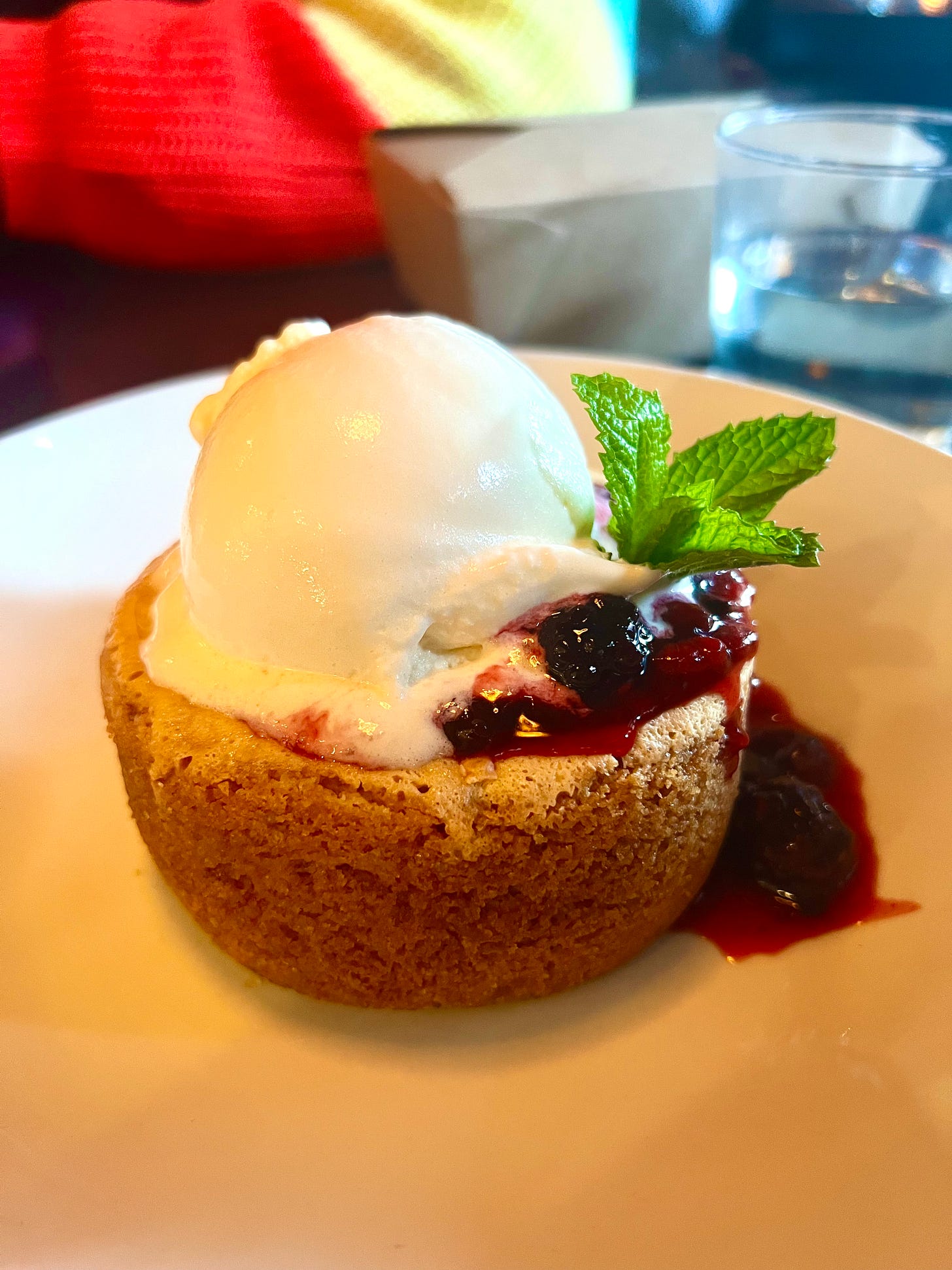 Scoop of ice cream on top of small round of butter cake with mint leaf and raspberries