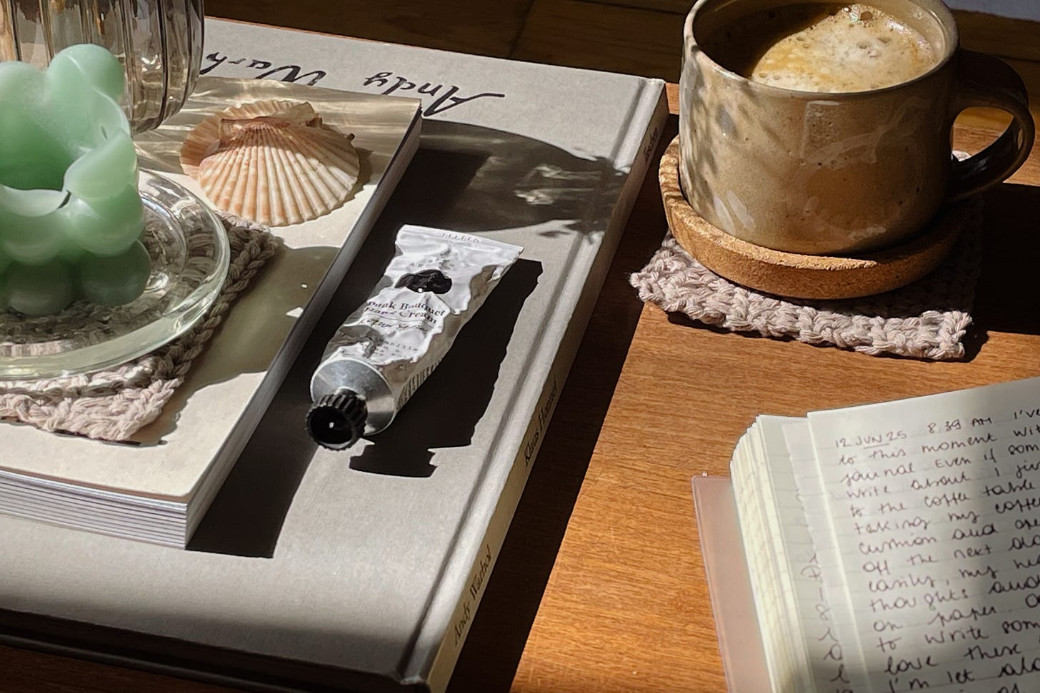 Coffee table with books, candle, seashells, hand cream, and a coffee mug near an open journal.