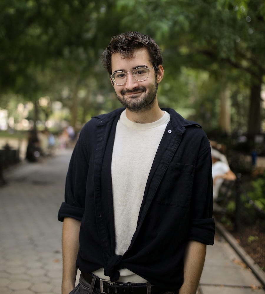 Photo of author Adam Aleksic, pictured outdoors on a park path in what appears to be New York City.