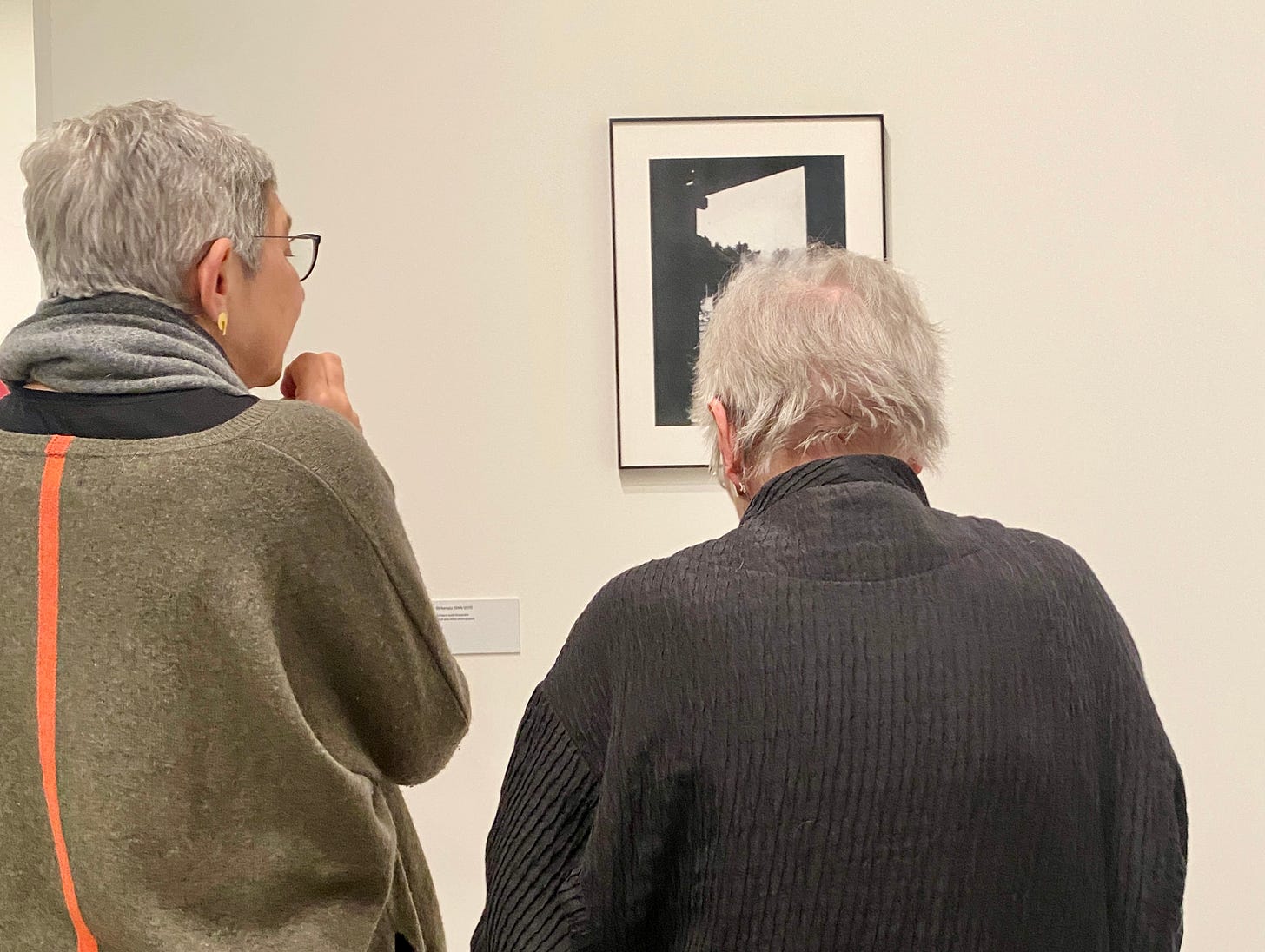 Duas senhoras de costas olhando para uma pequena fotografia preto & branca na parede Duas senhoras de costas olhando para uma pequena fotografia preto & branca na parede