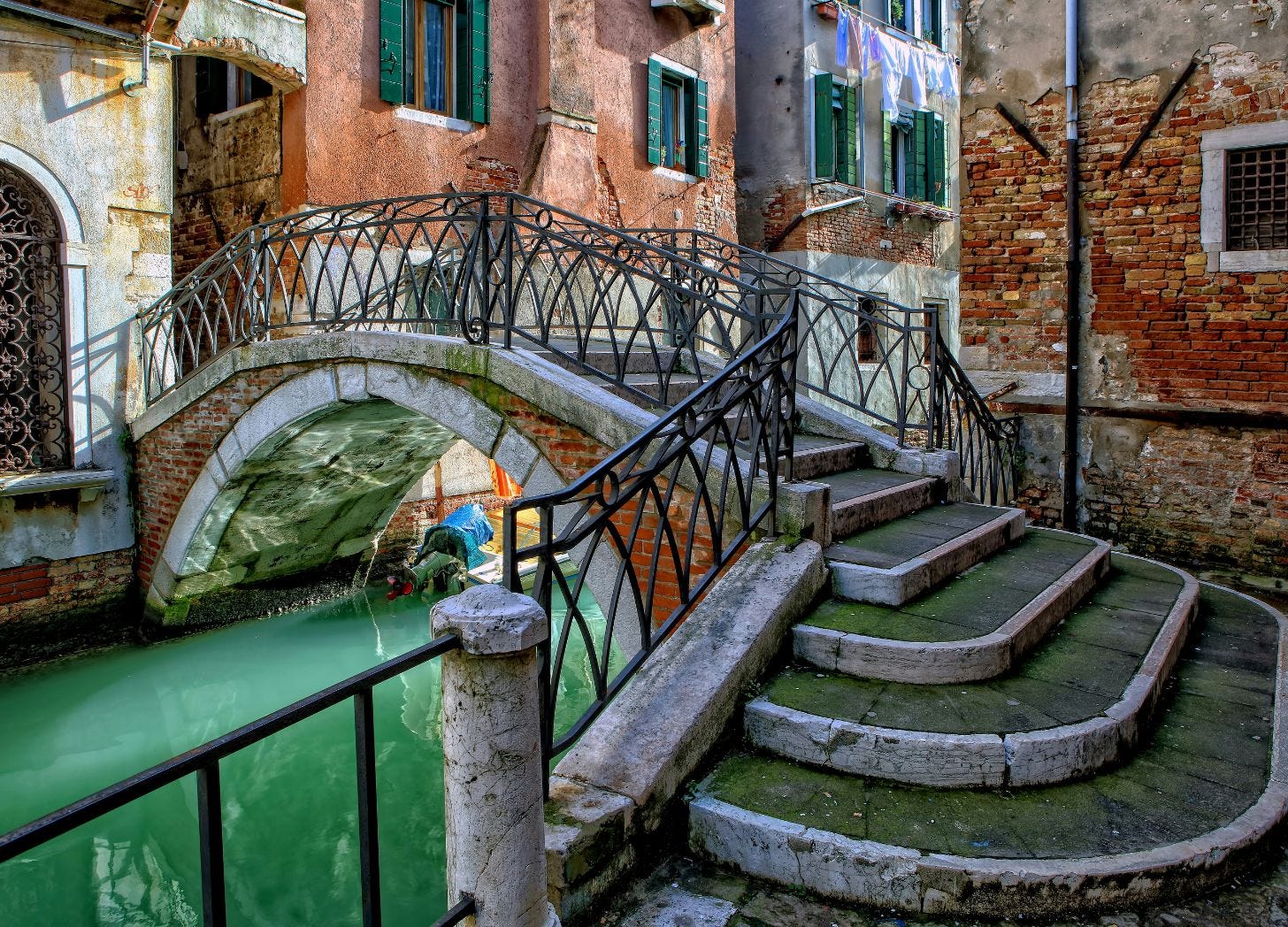 An empty bridge over a quiet Venice canal, with laundry hanging from windows and moss-covered stone steps—the texture of a place when there's room to breathe. An empty bridge over a quiet Venice canal, with laundry hanging from windows and moss-covered stone steps—the texture of a place when there's room to breathe.