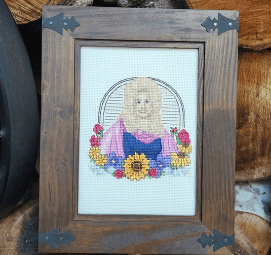 A framed cross stitch of Dolly Parton, highly detailed with florals and backstitch details.