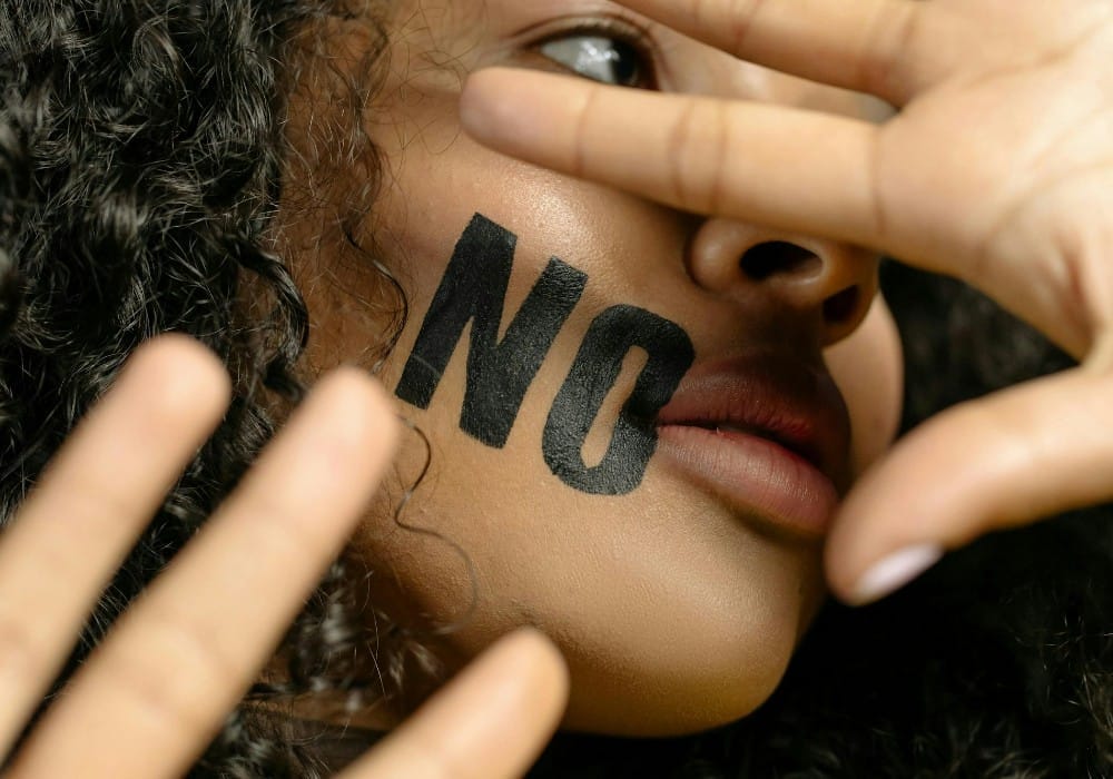 Young black woman with "no" stamped on her cheek in large black font