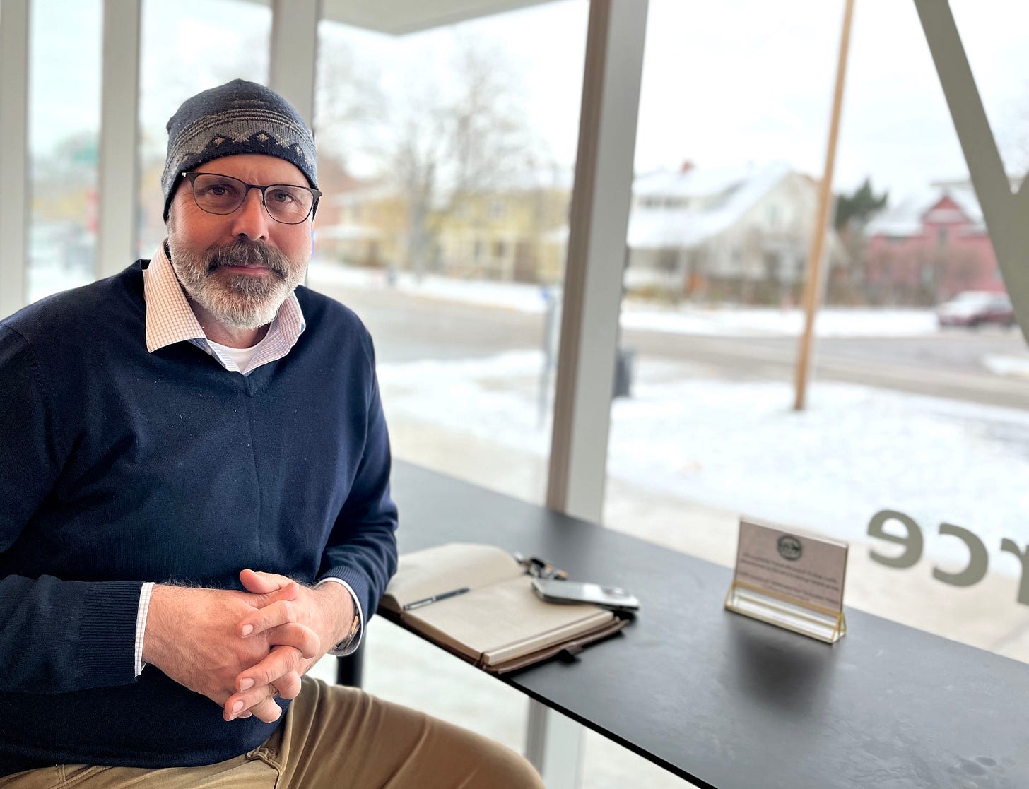 man in beanie at cafe bar with snow outside window