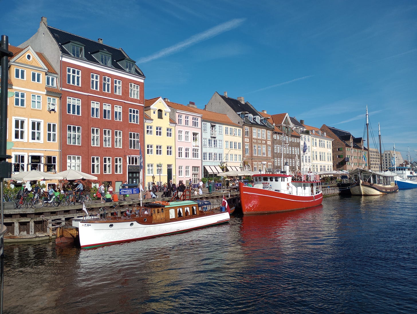 Colorful townhouses along a water byway in the Copenhagen, Denmark. Sidewalk cafes and boats, including a bright red one, line the harbor.