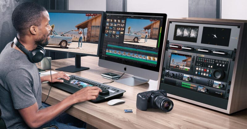 A man sits at a desk editing a video on a large computer; he wears headphones and uses a keyboard with colored keys. Nearby are a camera, an SD card, control panels, and two monitors displaying video footage. A man sits at a desk editing a video on a large computer; he wears headphones and uses a keyboard with colored keys. Nearby are a camera, an SD card, control panels, and two monitors displaying video footage.