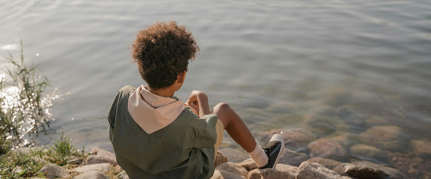 Boy sitting on the edge of a river, looking at the water