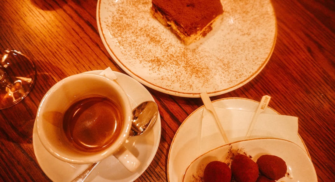 A wooden table with espresso, tiramisu, and truffles on it A wooden table with espresso, tiramisu, and truffles on it