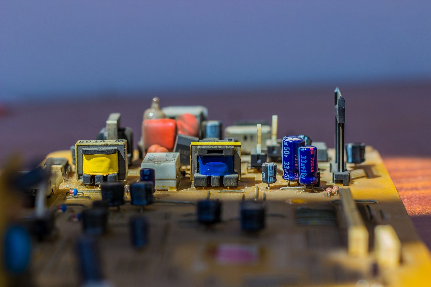 Inquadratura di un circuito e dei pezzi interni di un computer, con pezzi di diversi colori (giallo, rosso, blu, grigio, nero). Lo sfondo è sfuocato, con linee orizzontali di color malva e azzurrino. Inquadratura di un circuito e dei pezzi interni di un computer, con pezzi di diversi colori (giallo, rosso, blu, grigio, nero). Lo sfondo è sfuocato, con linee orizzontali di color malva e azzurrino.