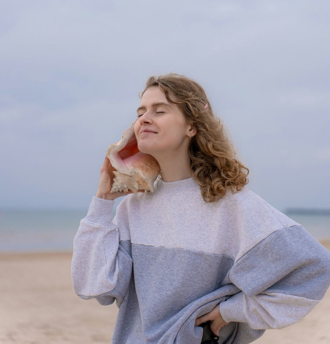 a woman standing on a beach holding a seashell a woman standing on a beach holding a seashell