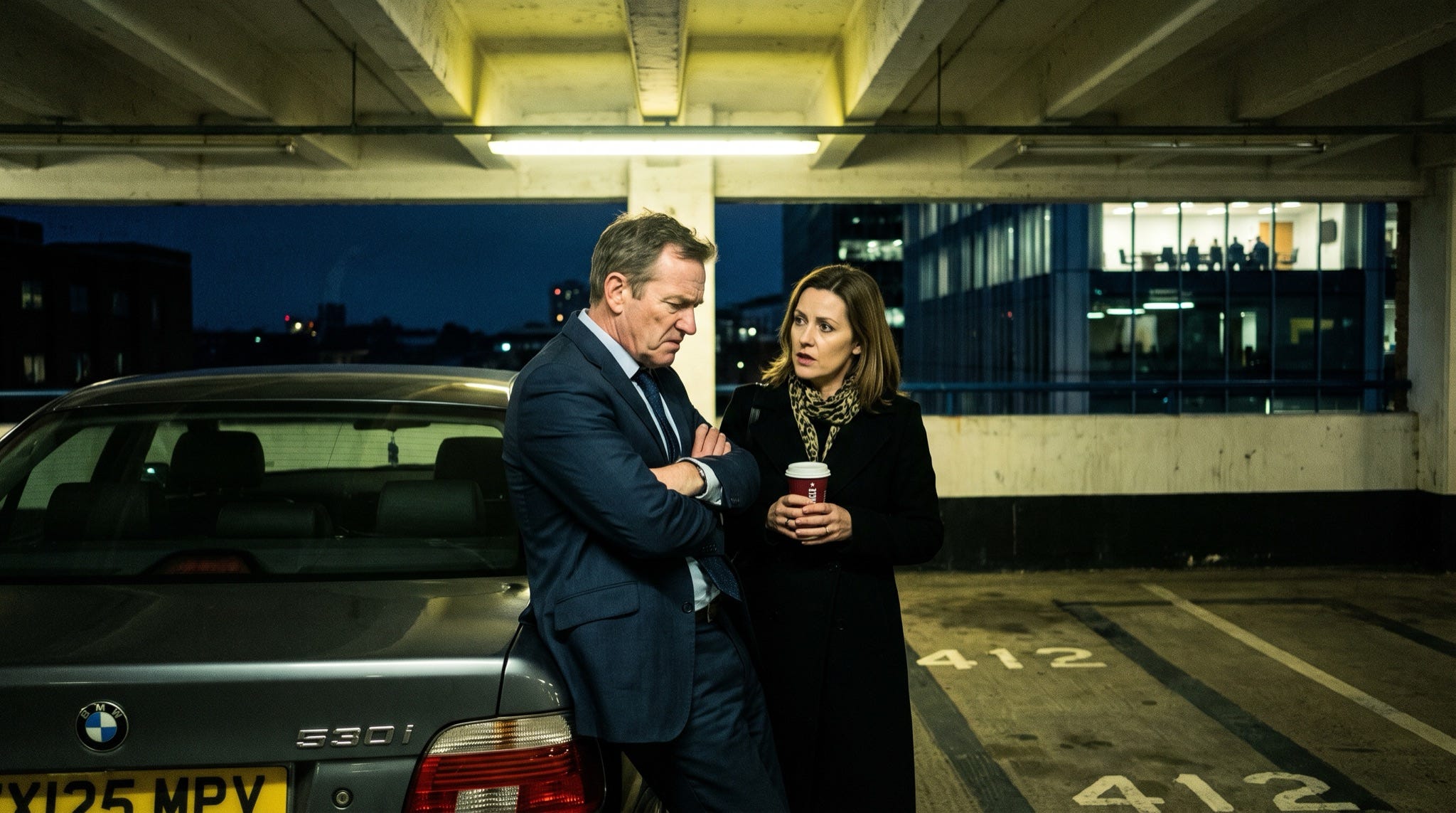 Two executives in business dress talking candidly beside a car at night in a concrete office car park, a lit boardroom still occupied visible through the glass tower behind them