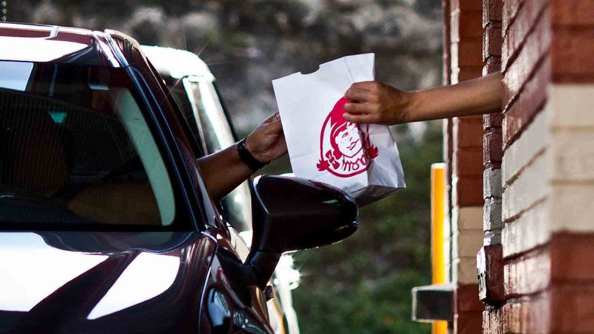 Wendy's employee handing an order to a drive through customer