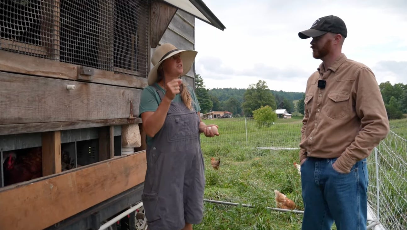 Elizabeth Collins talks with a visitor beside a mobile chicken coop, with pasture-raised chickens grazing in the background at Otter Creek Farms.