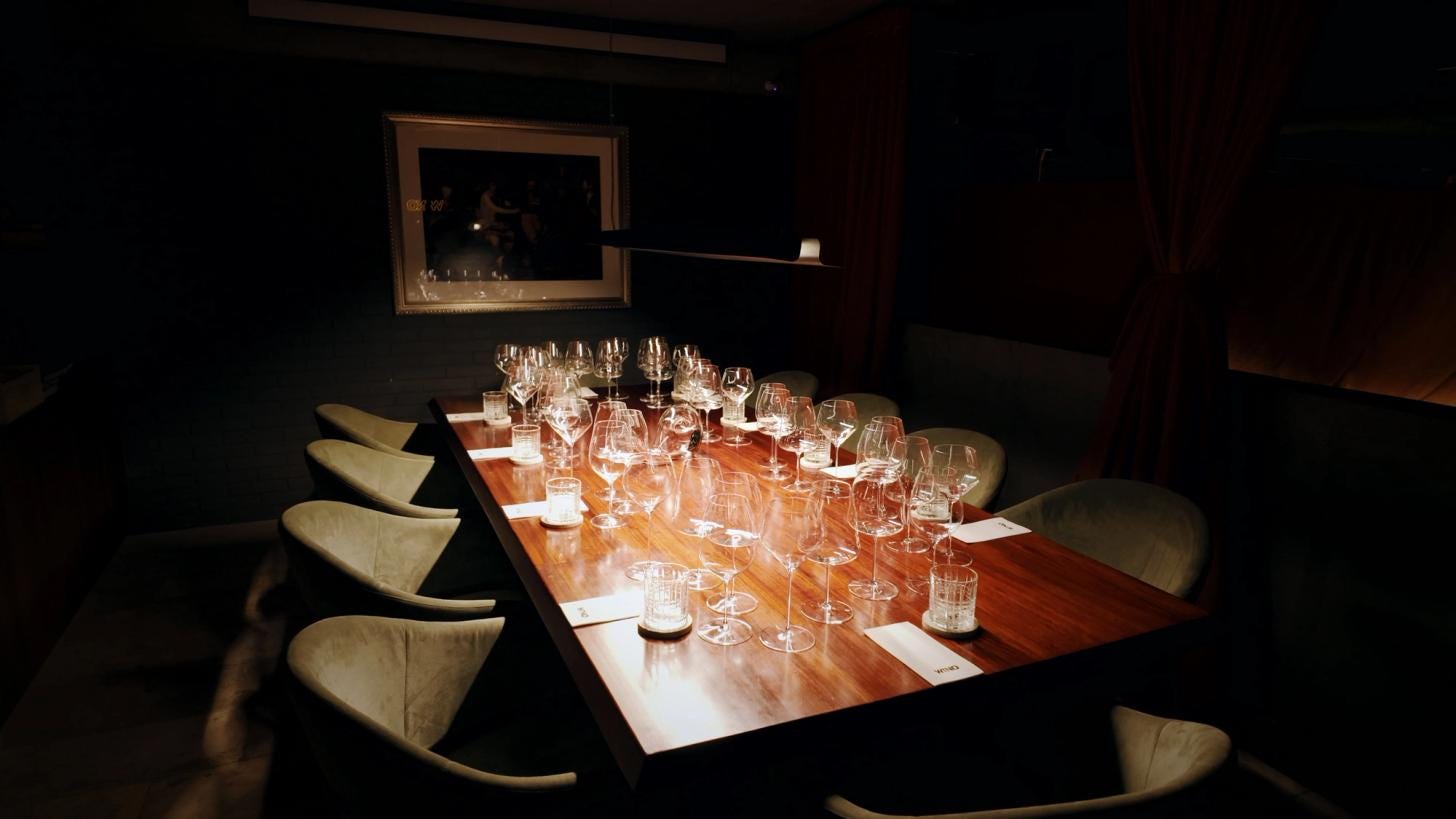 A private dining room beside the cellar: a long wood table set with tasting glasses, shelves of wine books along one wall. A private dining room beside the cellar: a long wood table set with tasting glasses, shelves of wine books along one wall.