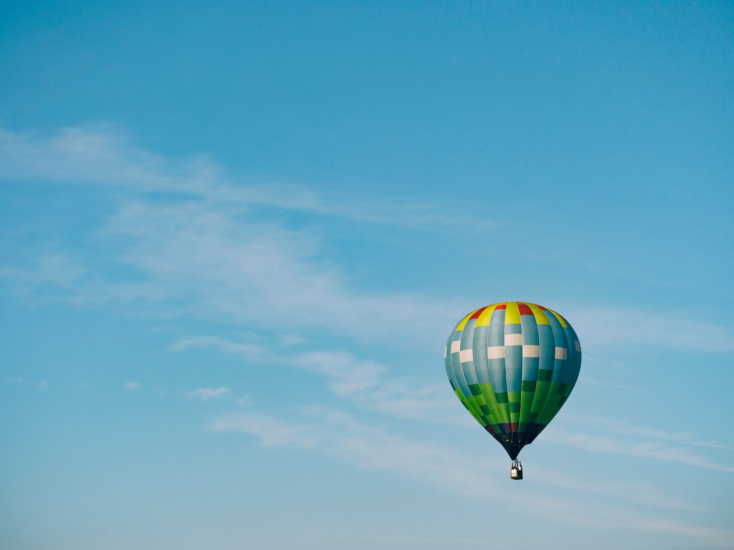 Photo of a blue, green, yellow and red hot air balloon flies in a clear blue sky.