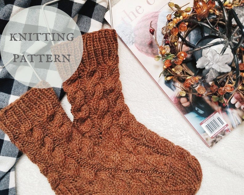May include: A pair of brown knitted socks with a cable knit pattern. The socks are displayed on a white surface with a black and white checkered fabric and a magazine in the background. The text 'KNITTING PATTERN' is displayed in a white circle on the checkered fabric.