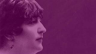 Retrato en perfil de una mujer con cabello corto y rizado, sobre un fondo de color púrpura. La imagen destaca su rostro, mostrando una expresión serena. Lleva un pendiente visible en una de sus orejas. La composición es minimalista y enfocada en su perfil.