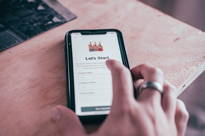 A picture of a hand reaching towards a phone with a mobile onboarding screen being shown. A picture of a hand reaching towards a phone with a mobile onboarding screen being shown.