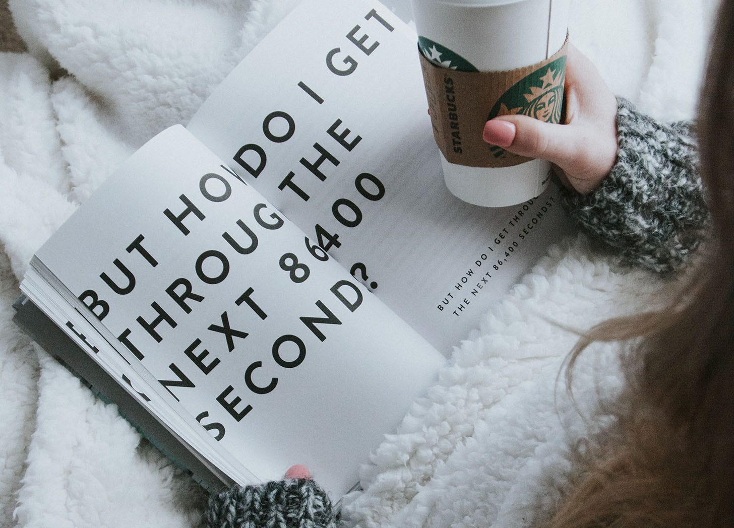 woman holding takeout coffee and reading a book that says in large print, "how to get through the next 86400 seconds." woman holding takeout coffee and reading a book that says in large print, "how to get through the next 86400 seconds."
