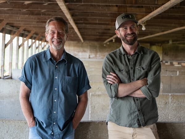 Rand Faaborg and Tanner Faaborg, both smiling widely as they stand in what appears to be a former hog barn. 
