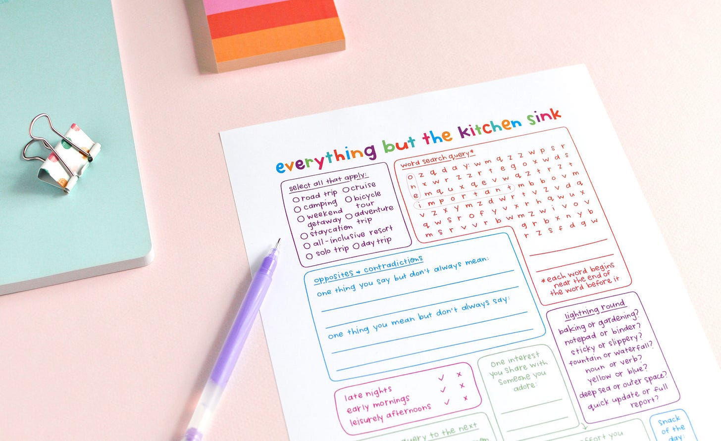 A colourful, hand-letter journal page titled Everything But the Kitchen Sink, filled with journal prompts and writing spaces. Shown with colourful notepad, notebook, binder clip and purple pen on a light pink background.
