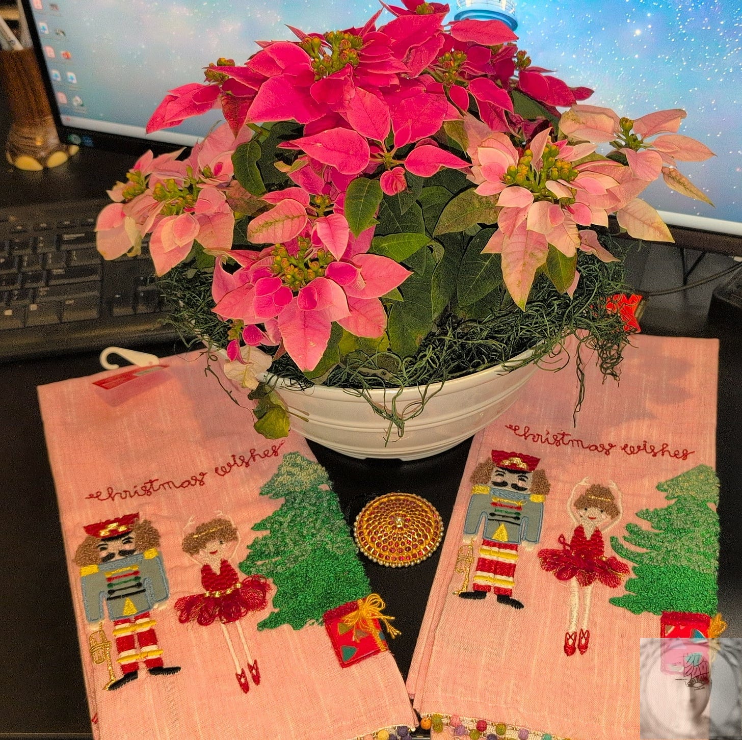 A white bowl of pink poinsettias, a Nutcracker and ballerina embroidered pink towel, and a ruby pendant